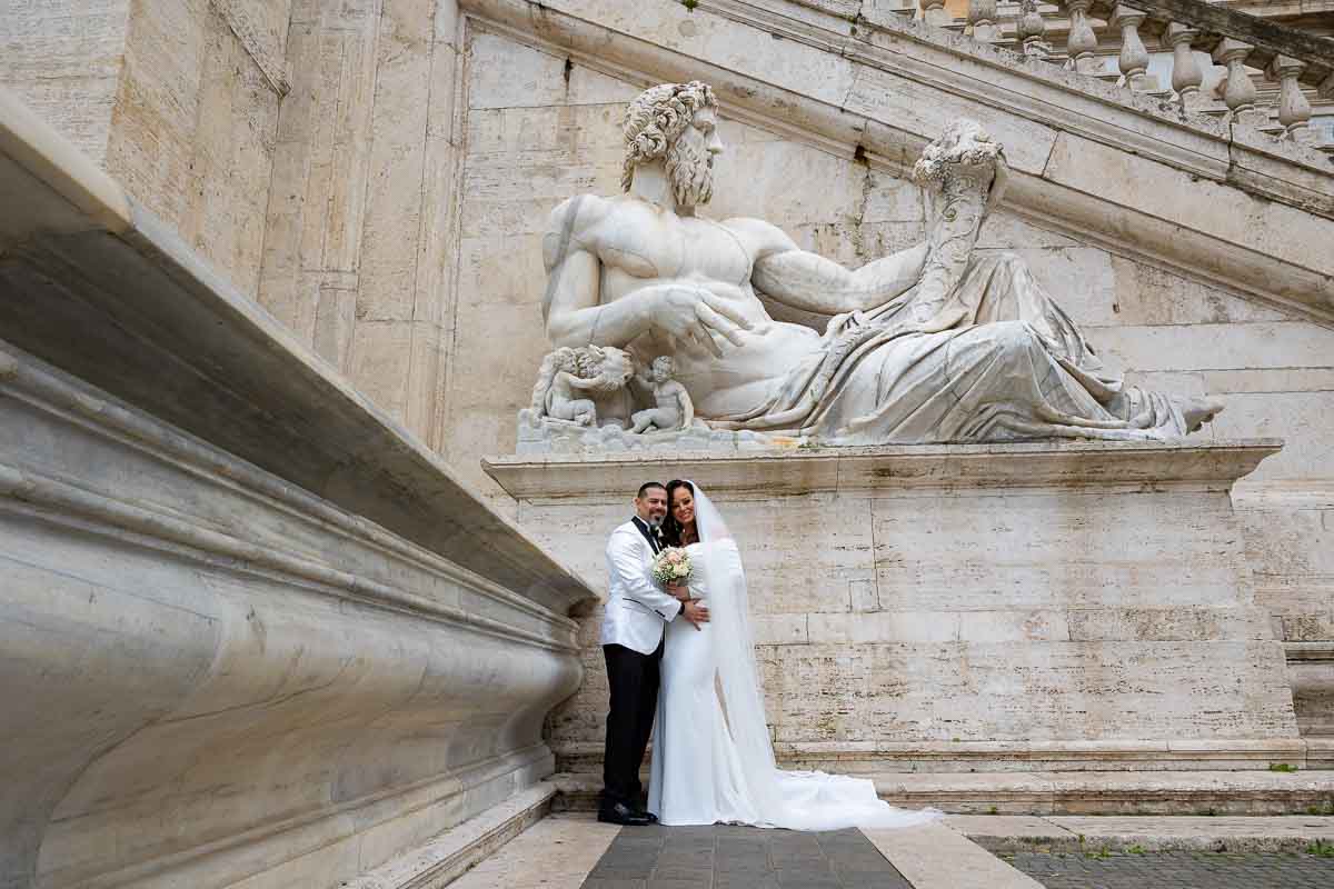 Wedding couple taking pictures underneath a roman marble statue