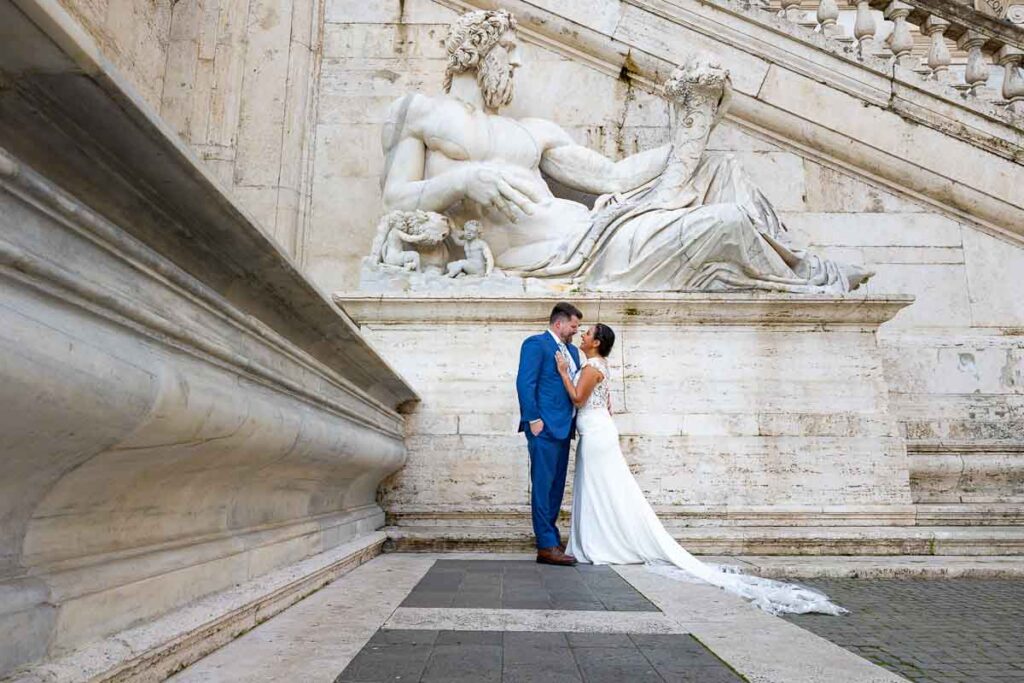 Wedding photography in Rome with the bride and groom standing beneath an ancient roman marble statue