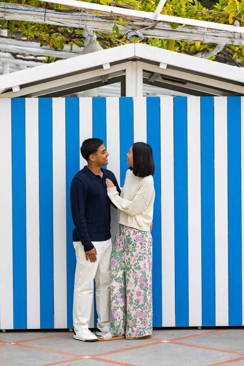 Couple posing in front of beach cabin with blue and white stripes typical of the summer season 