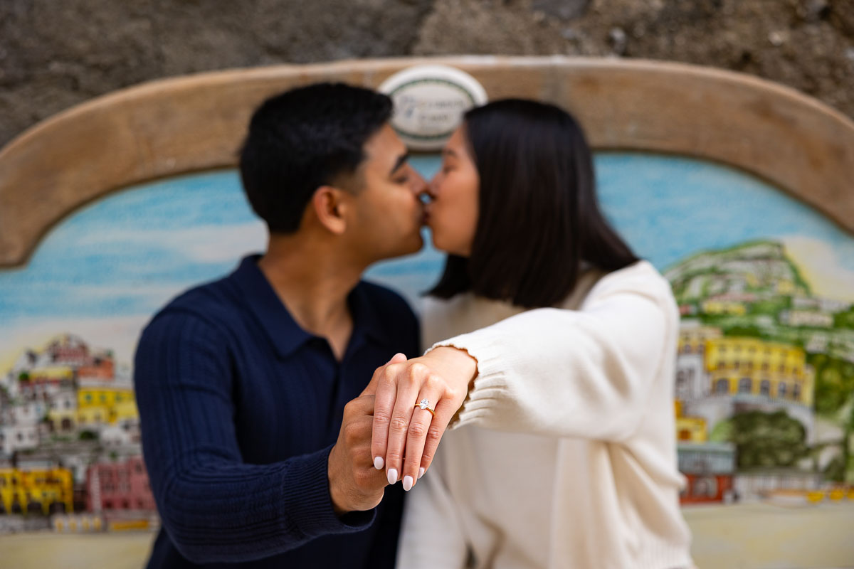Kissing with the engagement ring shown in the forefront and the couple kissing the background 