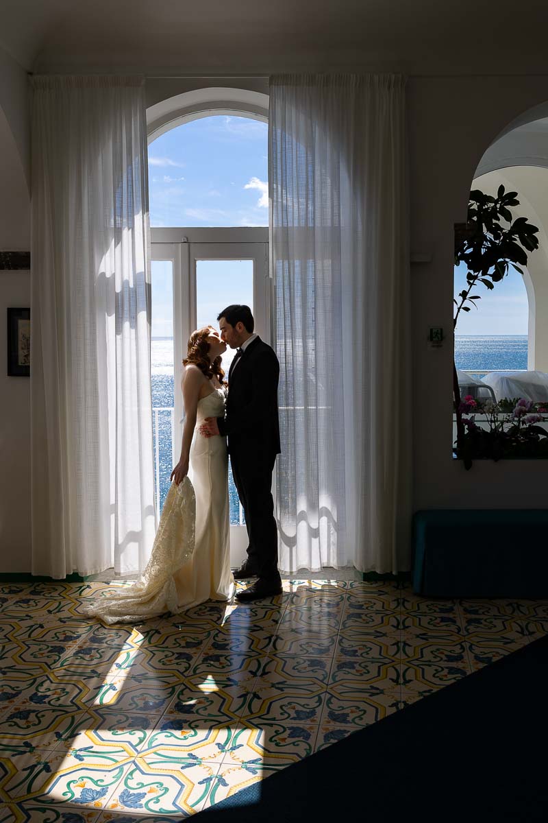 Bride and groom taking indoor photos by the window with nice natural light creating interesting photographic effects made of dark and light contrast areas