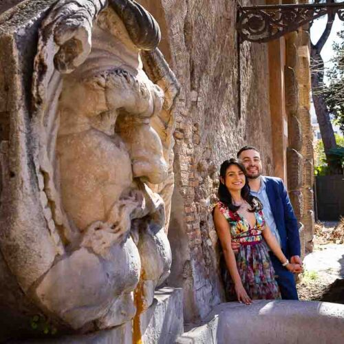 Portrait picture depicting a couple photographed by an ancient roman statue at the entrance of Giardino degli aranci