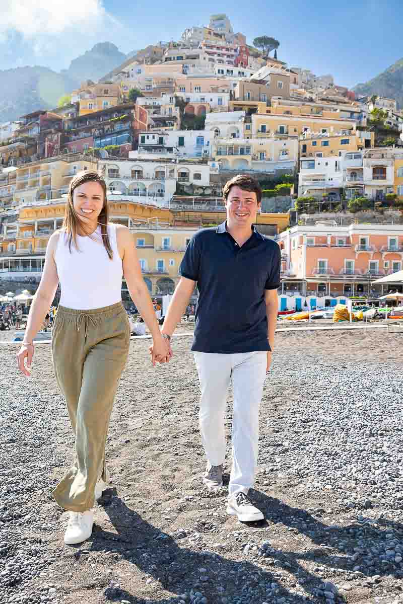 Walking hand in hand on the beach of Positano with the vertical town as a photographic background 