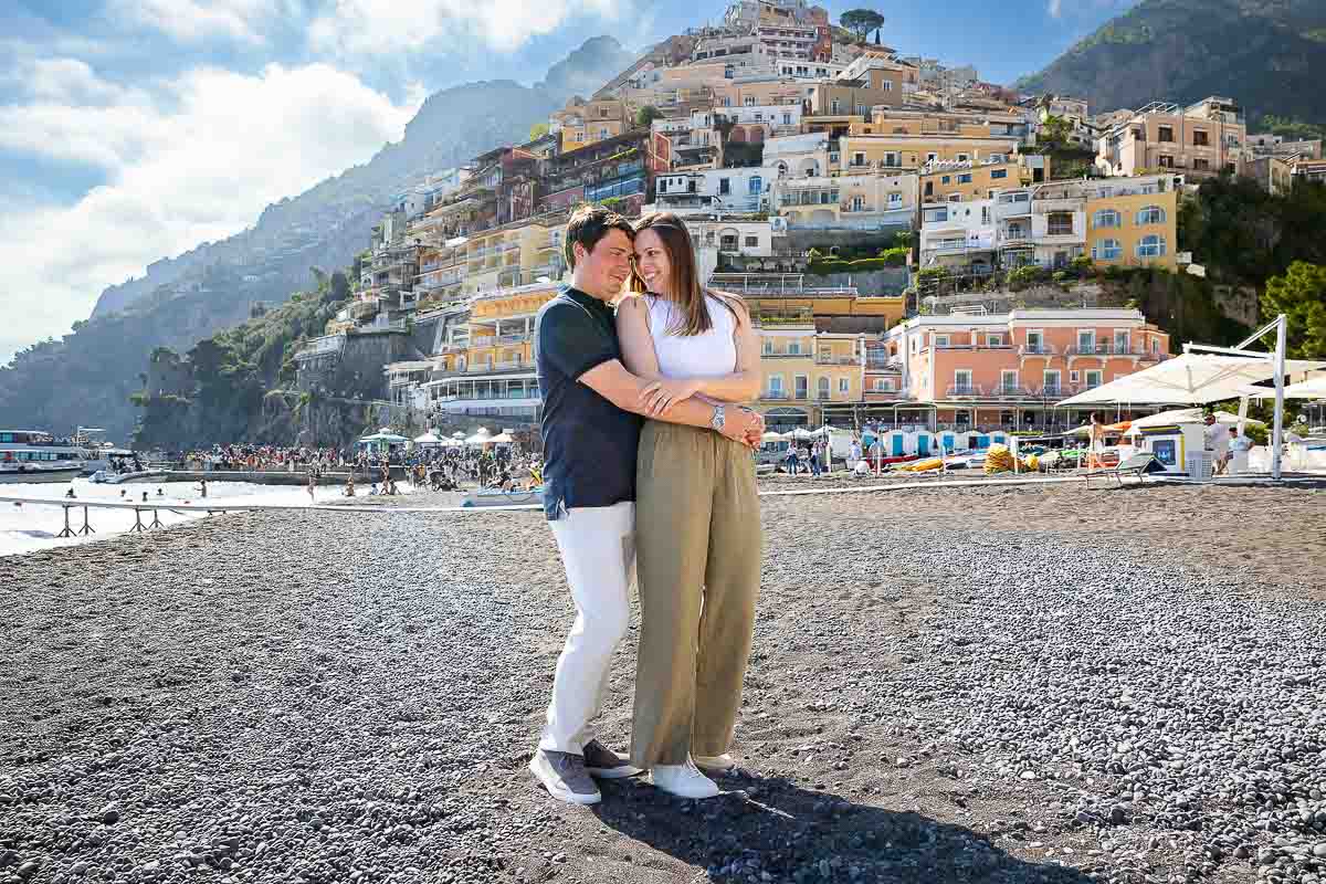 Couple posed close together holding each other while taking engagement photos on the beach of Positano Italy 