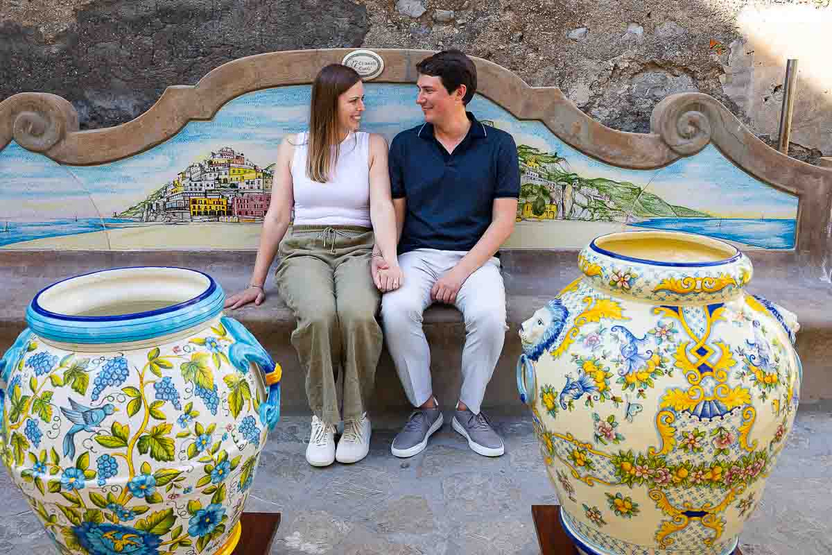 Sitting down in between ceramic vases while taking engagement pictures in the shade 