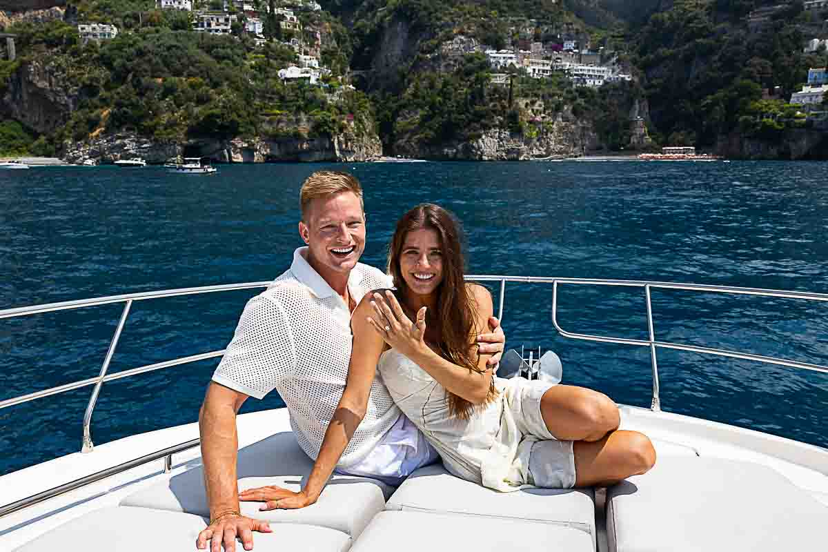 sitting down portrait pictures as just engaged on a boat near the coast of Amalfi in front of Positano