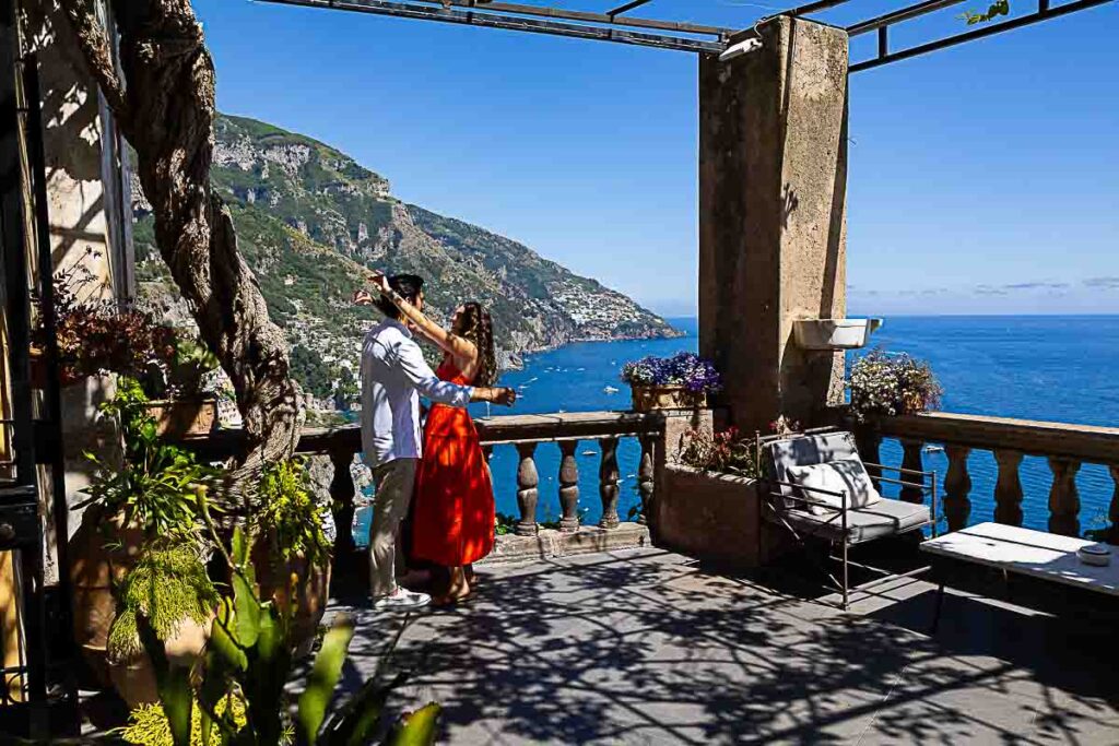 Wide-angle view of a couple celebrating their engagement on a panoramic terrace overlooking the southern Italian coastline