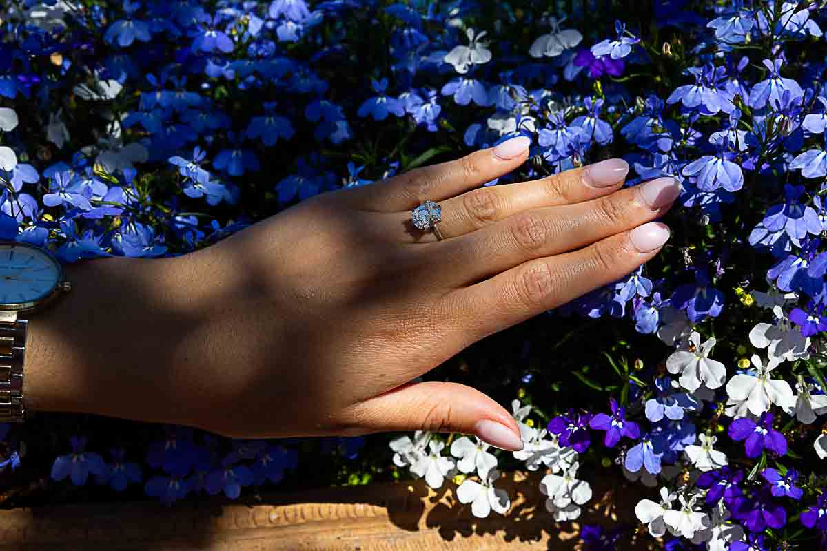 Artistic close-up of an engagement ring resting on soft blue blossoms, captured in a moody, low-light setting