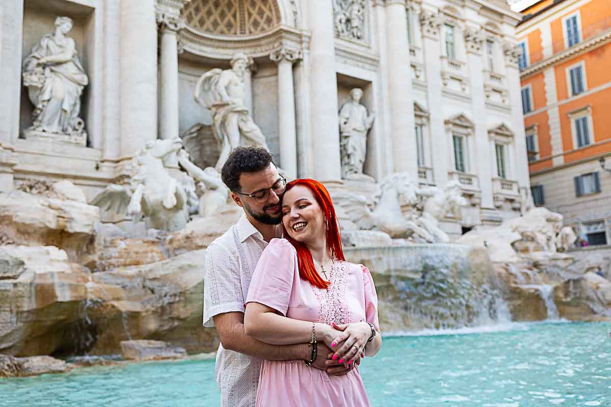 Couple at Trevi Fountain during sunrise photoshoot in Rome with golden light reflecting on the marble.