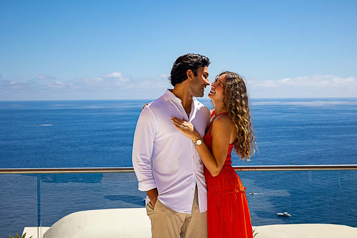 Posed couple gazing into each other’s eyes with a serene sea horizon stretching behind them, captured during a romantic photo shoot