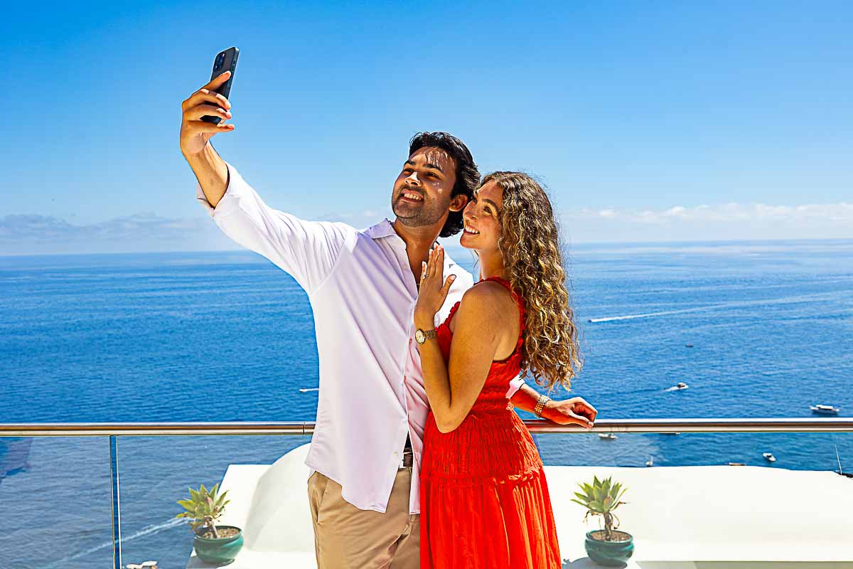 Couple taking a joyful selfie together during their engagement photo session by the coast