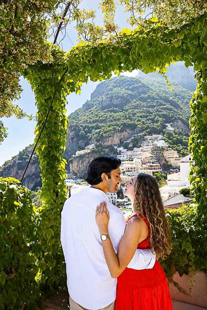 Couple in love gazing at each other, framed by delicate jasmine blooms with the colorful hillside town in the background