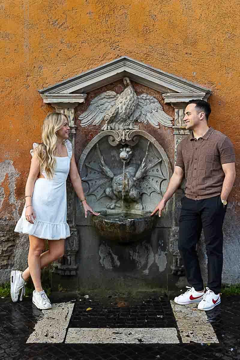 Posed portrait of a couple standing on either side of a water fountain on via della conciliazione 