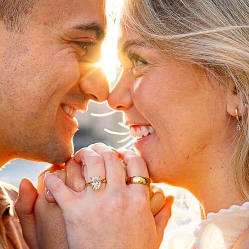 Close up sideways portrait of a couple at sun rising in the background with the engagement ring