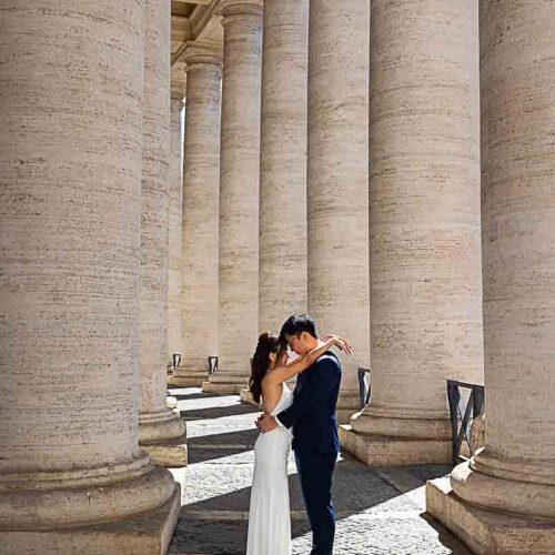 Rome wedding photo session color images taken underneath the vatican columns with light shining through the sides