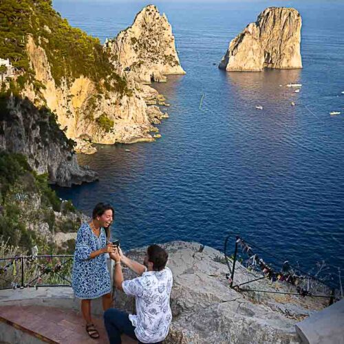 Kneel down surprise wedding marriage Capri engagement proposal on the Augustus Gardens with a stunning view of the faraglioni rocks in the far distance