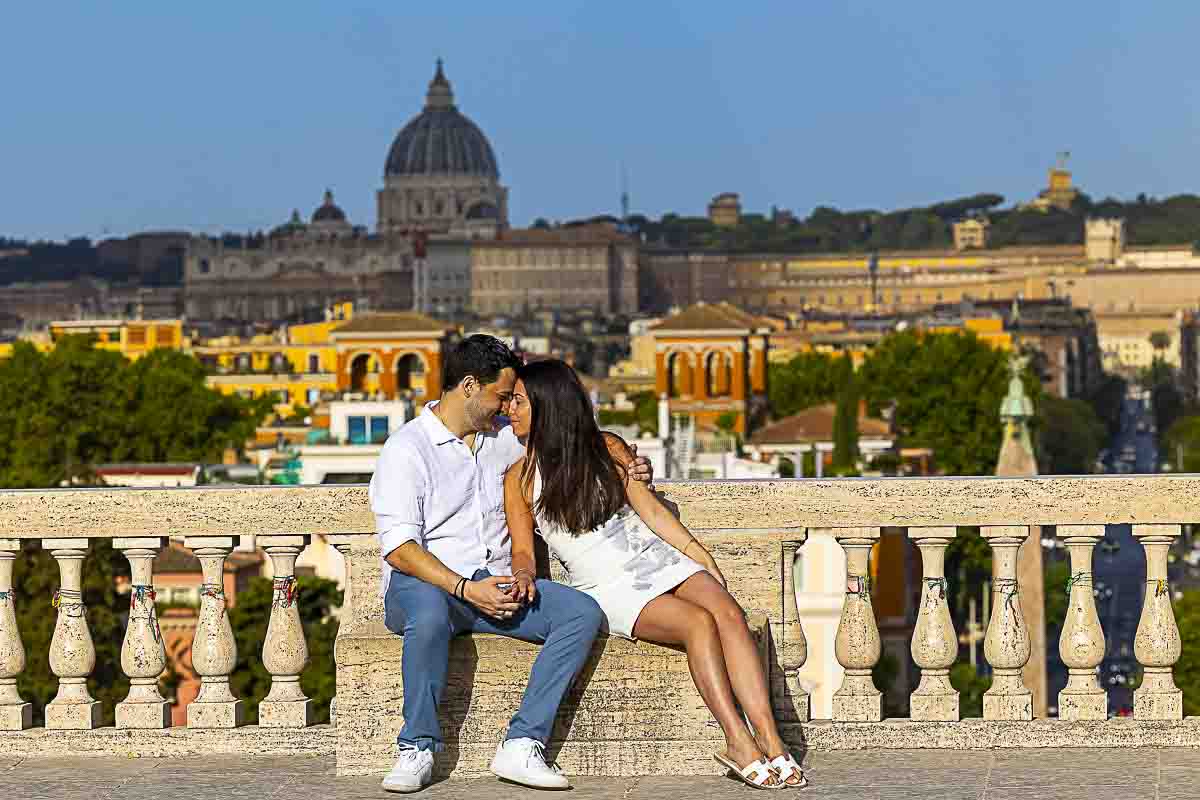 Posed snapshot while sitting on a marble bench right in front of the roman cityscape as the couple stands next to one another for engagement photos