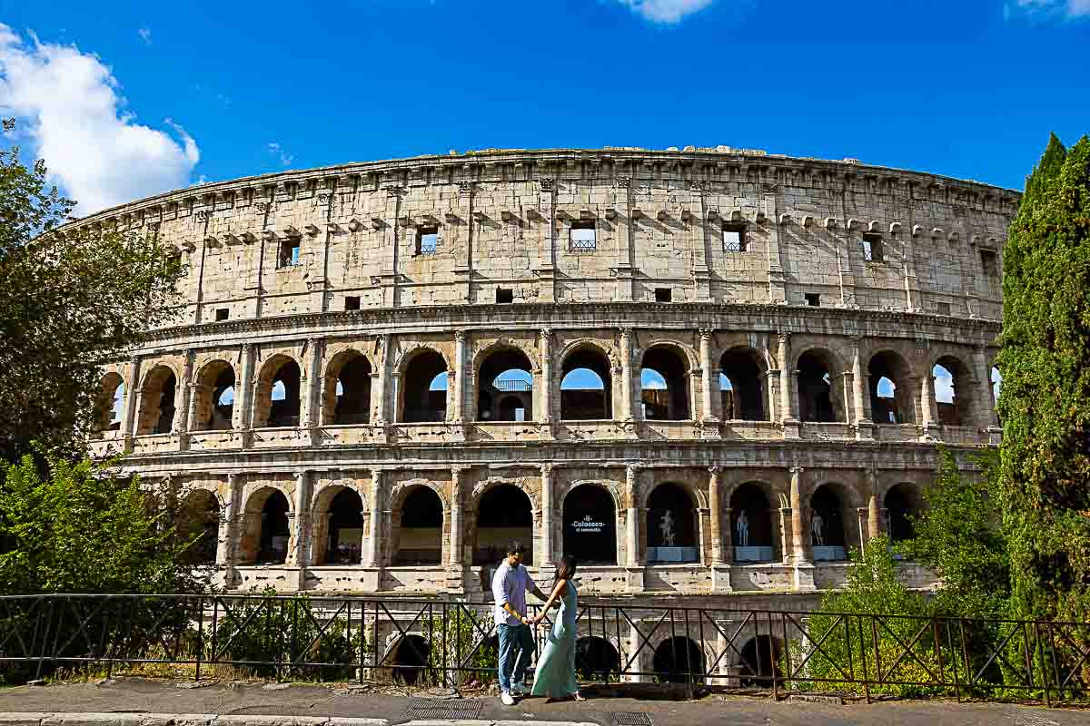 View of the Coliseum seen as wide angle with the couple standing beneath it walking and holding hands