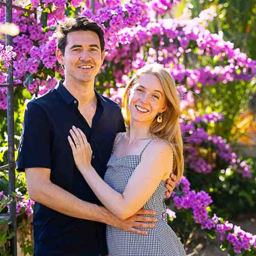 Posed before a bougainvillea fuchsia flower plant smiling and posing in front of the camera taking photos during a photoshoot in the park