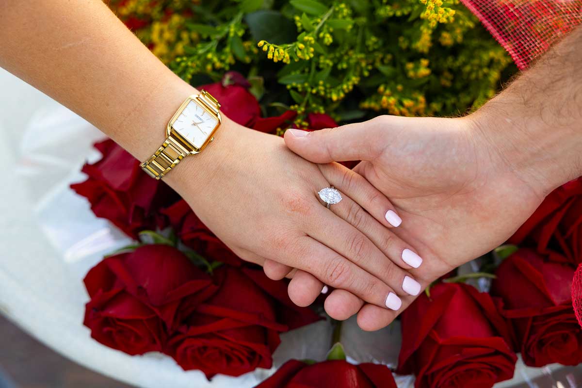 Engagement ring shot worn on the hand of the fiancee photographed while over red roses 