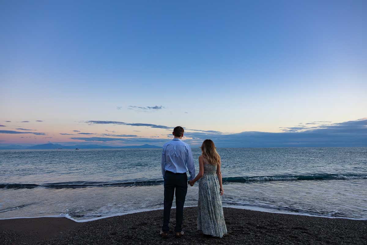 Looking together into the distance holding hand by the coast and the horizon during a photographer session with seascale at their feet 