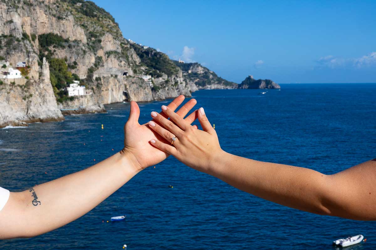 Hands holding each other with the engagement ring over the ocean water 