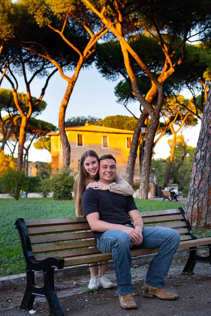 Taking couple photos while sitting down on a bench with trees up above and sunsetting light