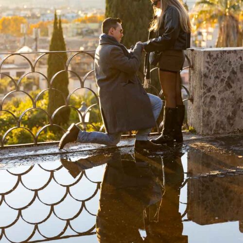 Proposing in Rome at the Pincio terrace panoramic outlook in front of a water puddle reflection and the typical metal fence