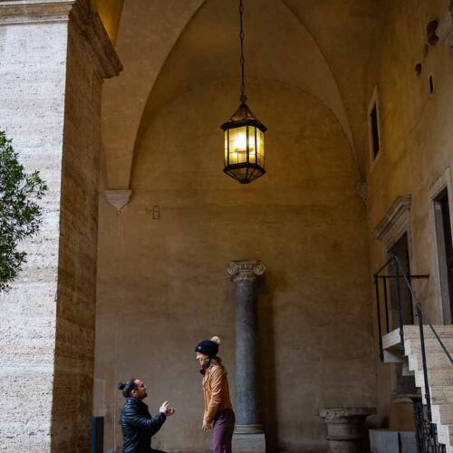 Roman Proposal in Rome Italy knelling down to ask the big question underneath a portico with beautiful natural light shining through