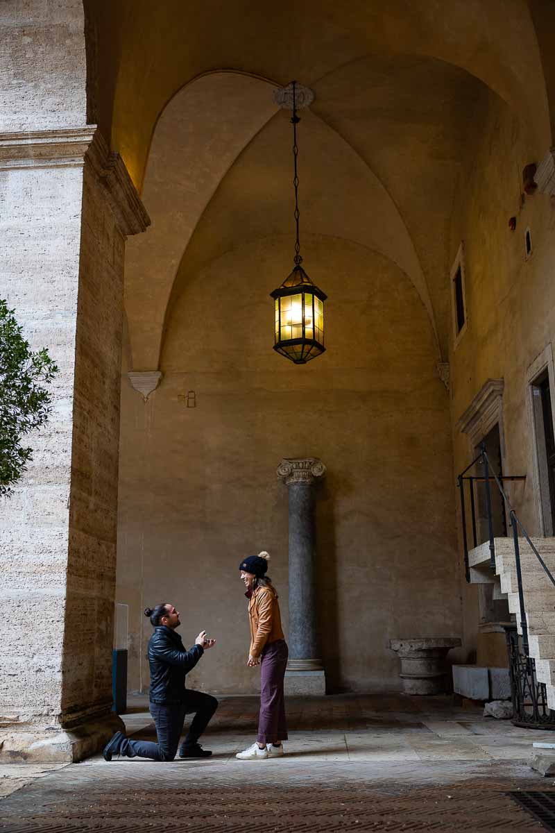 Rome Proposal in roman setting Italy kneeling down to ask the big question underneath a portico with beautiful natural light shining through 