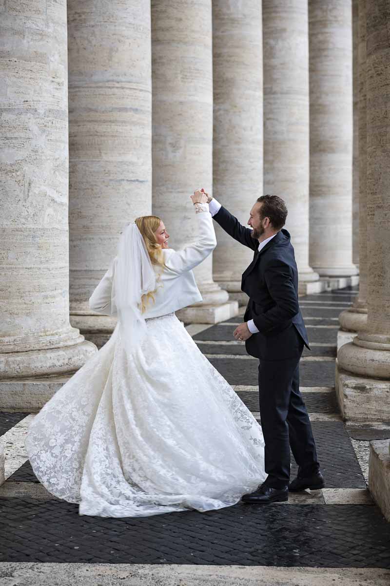 Groom twirling the bride under the vatican colonnade during a photoshoot in matrimonial attire 