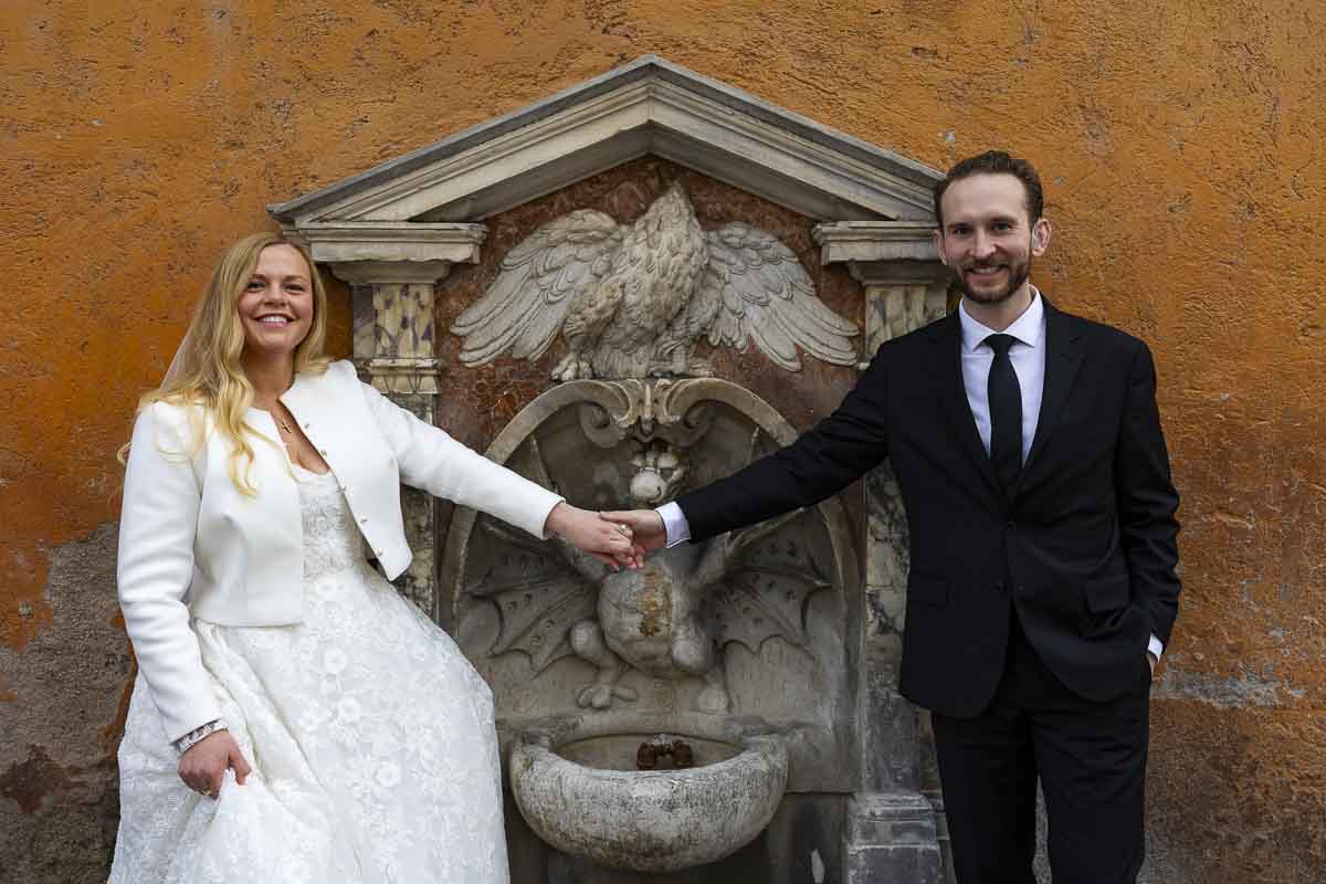 Reaching out to one another with their hands to take wed photos in front of vatican water fountain 