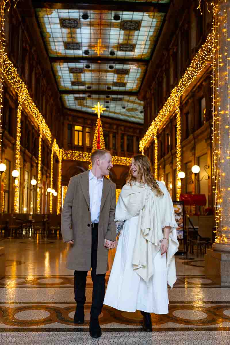 Couple walking inside Galleria Alberto Sordi surrounded by marble floors, Christmas lights, and early winter calm in central roman city.