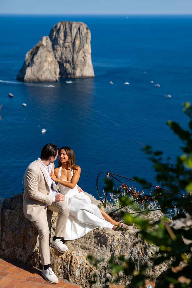 Subjects sitting down on a walled terrace taking pictures with the sea in the background 
