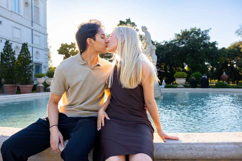 In love picture of a couple kissing at sunset golden hour during an engagement photoshoot by the water fountain