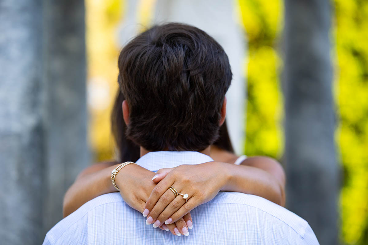 Engagement ring photo taken while she has her hands around his neck from behind 