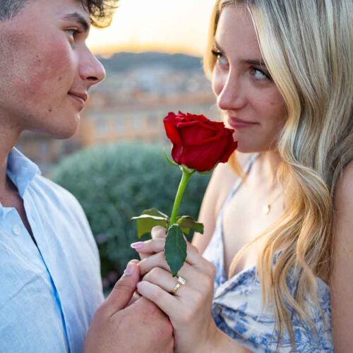 Nice image of a couple looking at each other while holding a rose and taking pictures during a photographer session