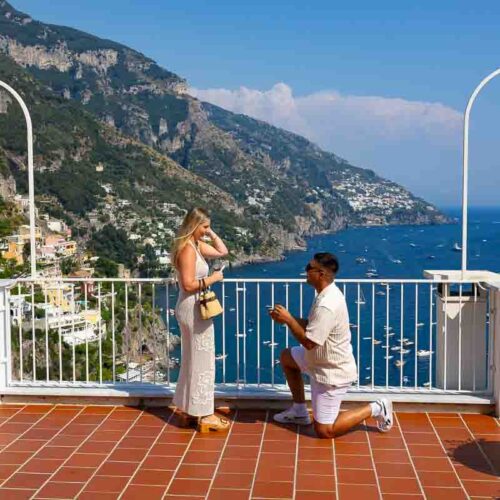 Private marriage proposal in Positano with the groom-to-be down on one knee and the Amalfi Coast stretching across the sea behind the couple
