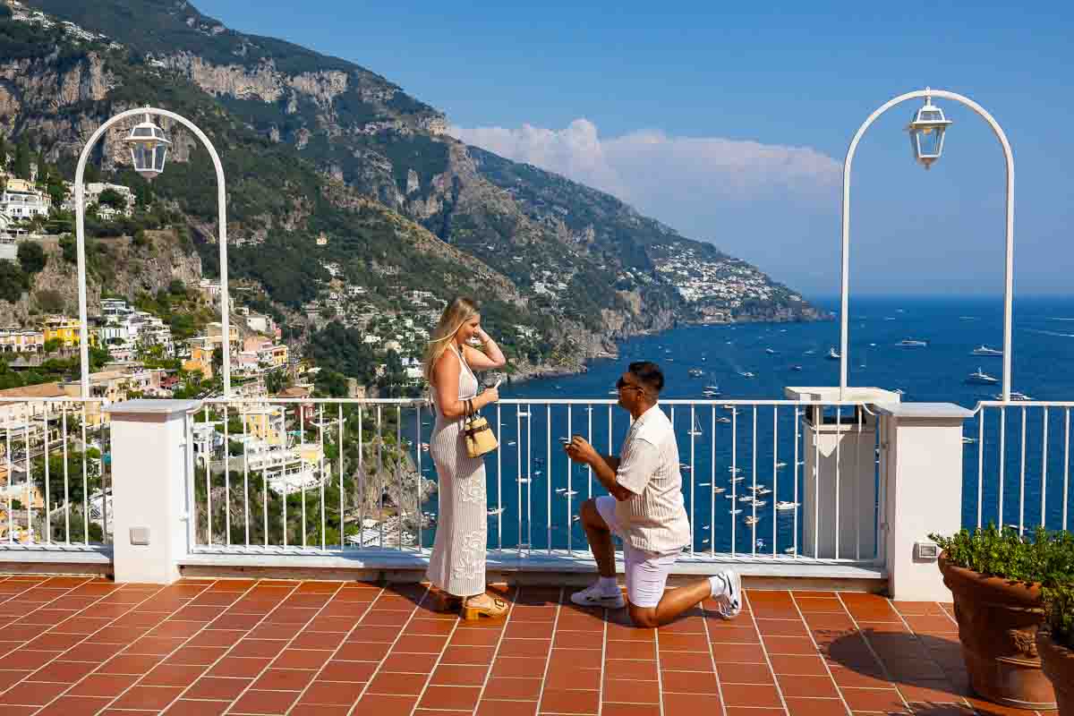 Private marriage proposal in Positano with the groom-to-be down on one knee and the Amalfi Coast stretching across the sea behind the couple