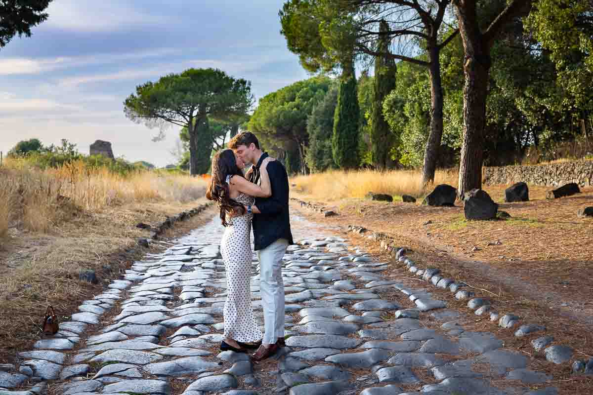 Newly engaged couple sharing a kiss while standing on massive weathered paving stones during an intimate portrait session