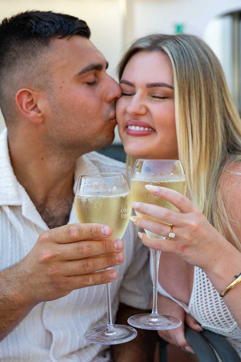 Newly engaged couple celebrating a romantic moment with prosecco and sparkling wine on a scenic rooftop overlooking the Mediterranean