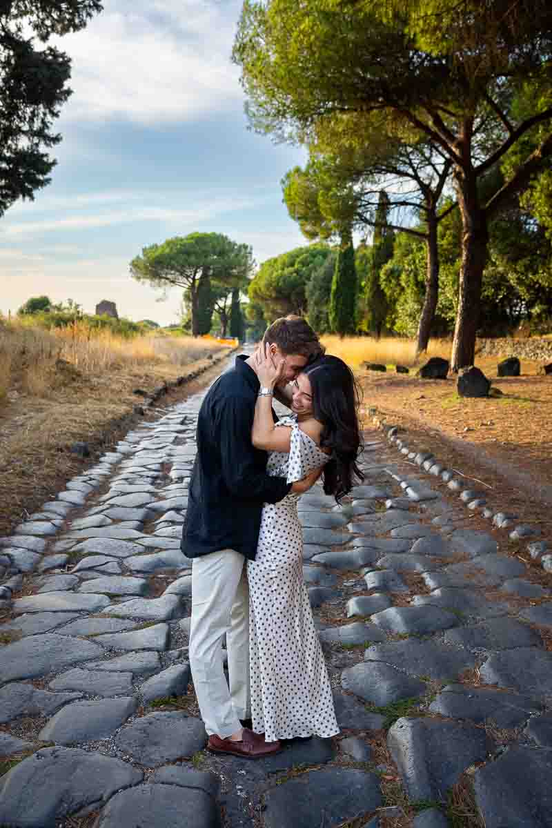 Romantic embrace and kiss along a historic Roman thoroughfare during a natural couples photo session surrounded by countryside