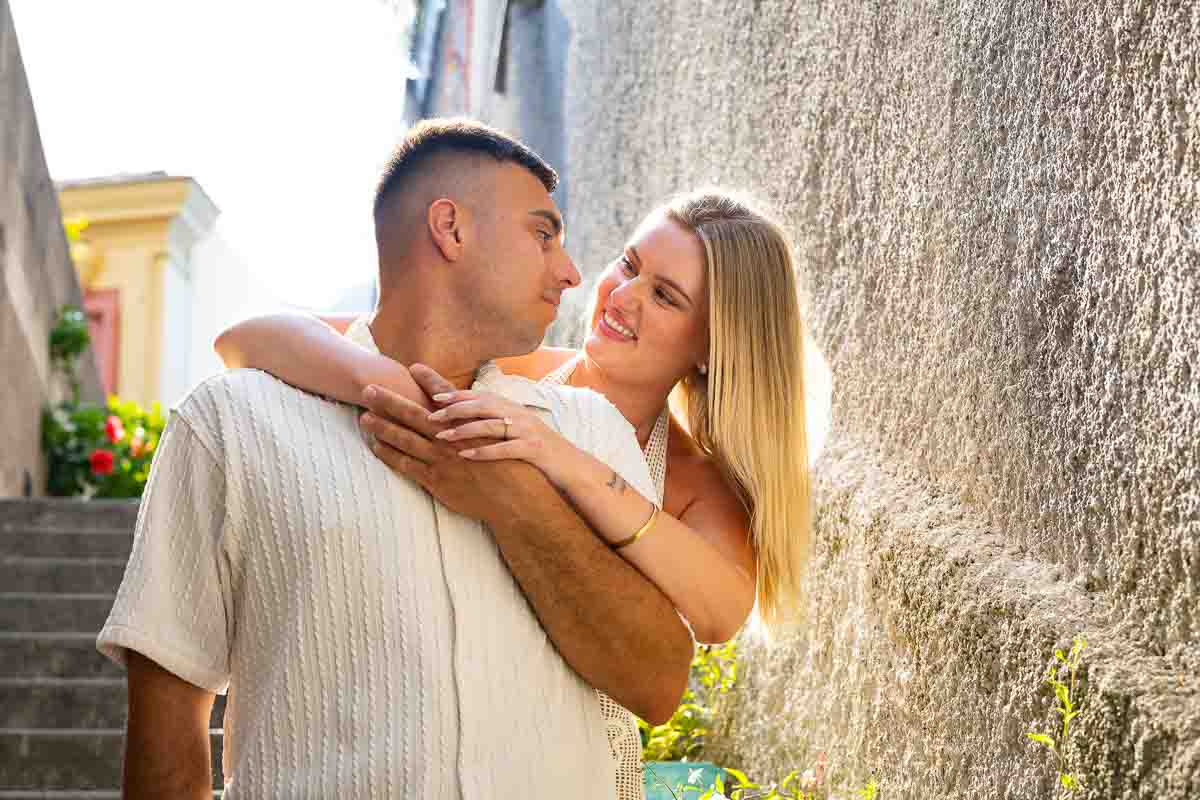 Engaged couple embracing on a historic staircase as warm sunlight filters through her hair during a natural couples portrait session