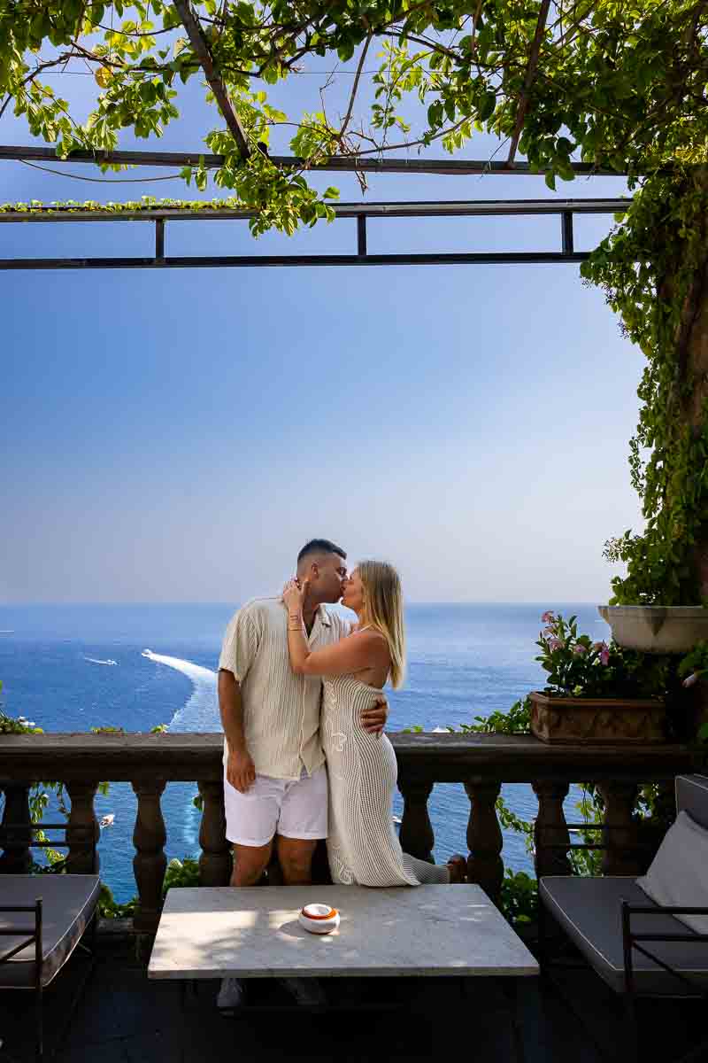 Couple photographed together on a scenic balcony overlooking the Mediterranean Sea, enjoying panoramic coastal views during their engagement photoshoot