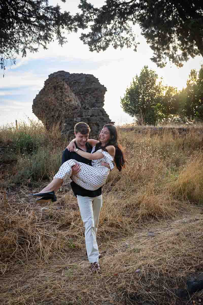 Playful moment as he carries his partner from the dry grass back onto the historic stone path during their portrait experience