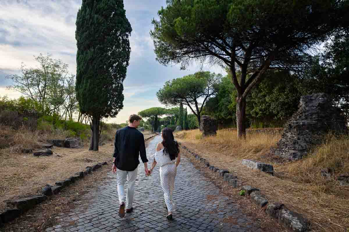 Couple walking hand in hand into the distance along a secluded country lane, photographed during their romantic engagement session