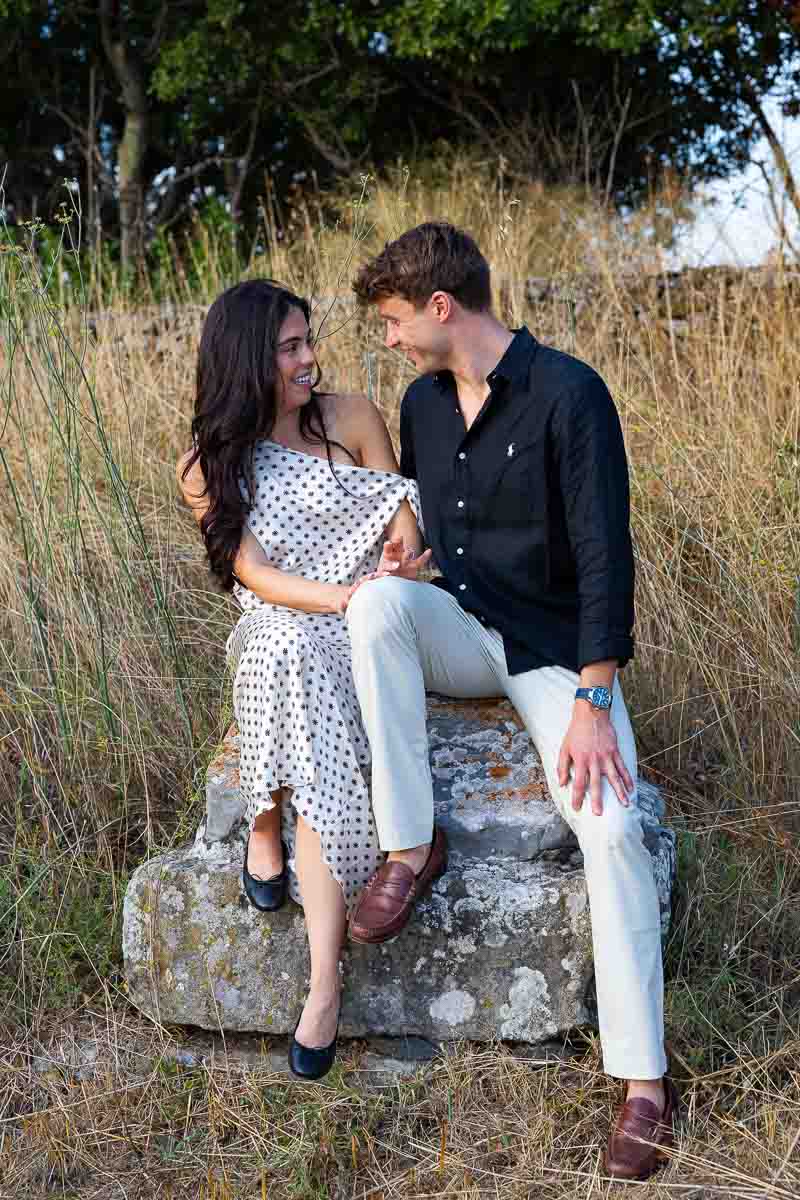 Newly engaged partners sitting together on preserved marble remains dating from the Roman era during a historical portrait shoot