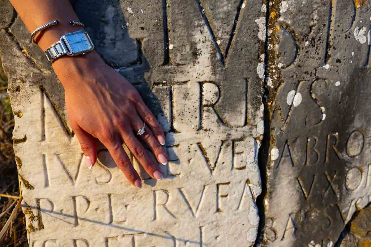 Diamond ring resting over ancient Latin inscriptions carved into marble, creating a distinctive historical detail photograph