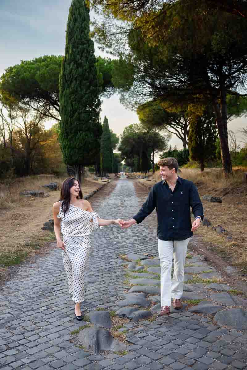 Joyful partners walking hand in hand and laughing together while exploring the historic landscape during their couples photo session