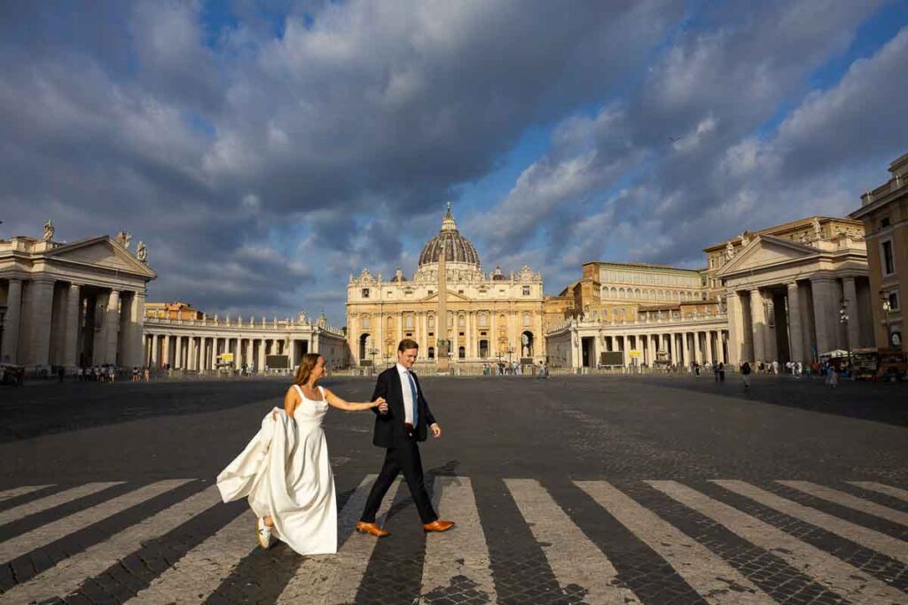 Pair crossing Via della Conciliazione hand in hand, with St. Peter’s Basilica in the distance forming the backdrop for this Rome street photograph
